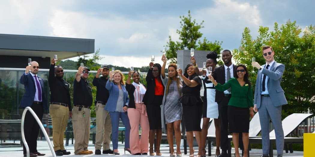A group of Bozzuto professionals standing on a poolside & raising wine glasses for a toast.