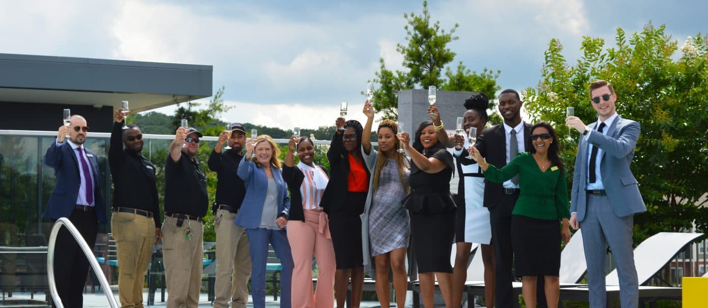 A group of Bozzuto professionals standing on a poolside & raising wine glasses for a toast.