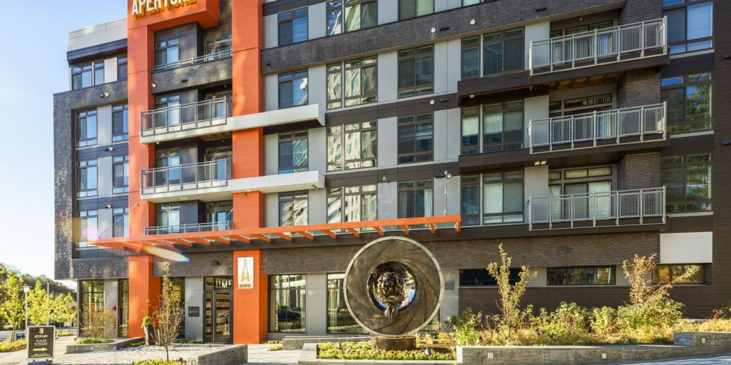 Building front of Aperture apartments featuring landscaping and a statue