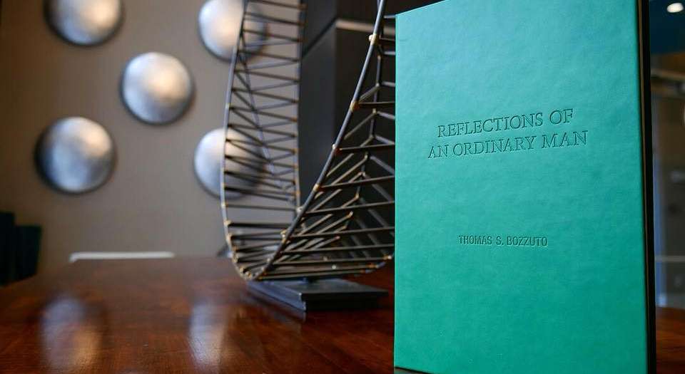 Thomas Bozzuto's green-covered book Reflections of an Ordinary Man on a table, with metal sculpture on the background.