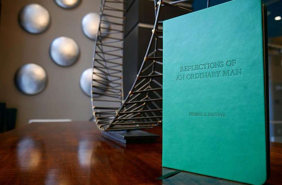 Thomas Bozzuto's green-covered book Reflections of an Ordinary Man on a table, with metal sculpture on the background.