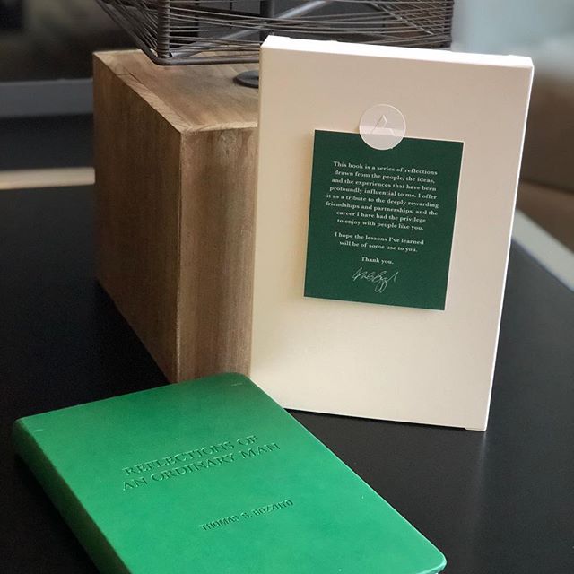 Tom Bozzuto's book titled 'Reflections of an Ordinary Man' resting on a table beside a white box & wooden decor