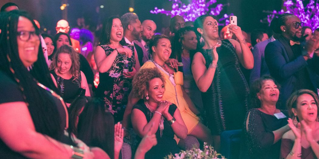 A diverse crowd gathered at a Bozzuto event, with one woman holding a camera phone.