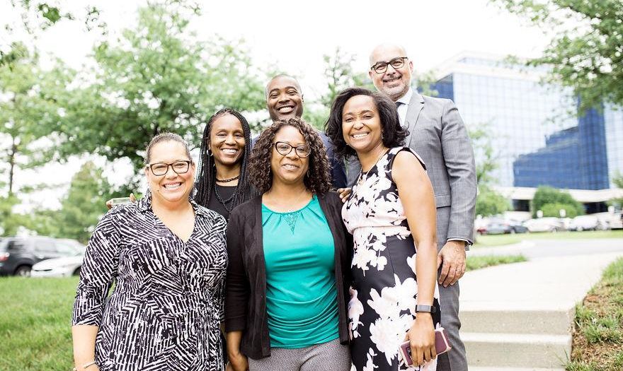 A diverse group of individuals standing on steps in front of a Bozzuto building.