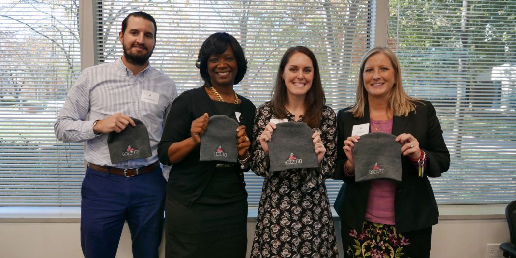 Four people in a Bozzuto office, each holding a beanie.