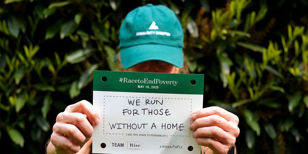 A man in a green Bozzuto cap holds a sign saying We run for those without a home.