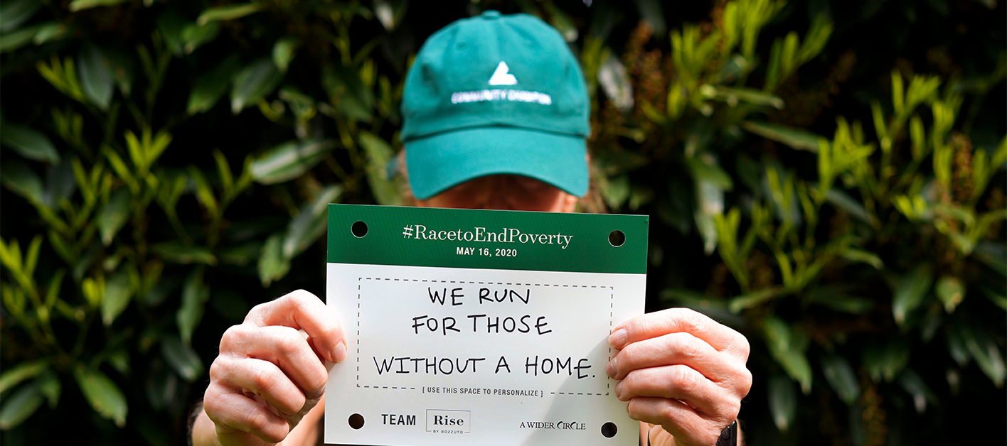 A man in a green Bozzuto cap holds a sign saying We run for those without a home.