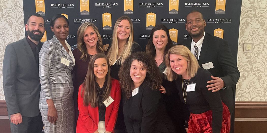 Smiling group of Bozzuto representatives posing in front of a Baltimore Sun Top Workplace banner.
