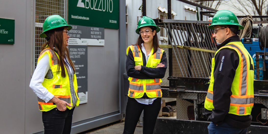 Three Bozzuto individuals in safety vests & hard hats in front of the field office.
