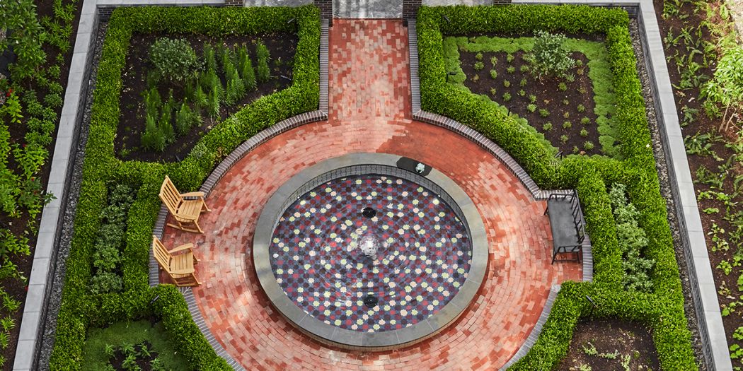 Aerial view of garden with fountain, surrounded by lush greenery and colorful flowers.