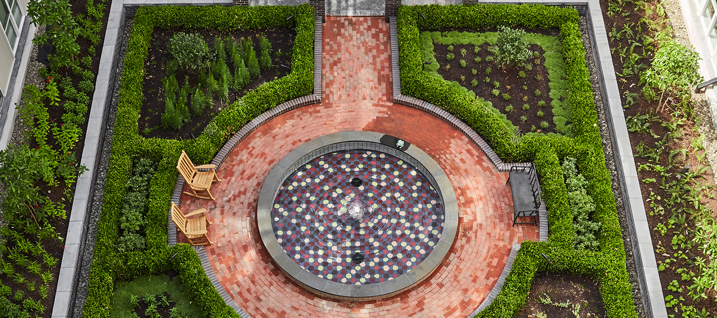 Aerial view of garden with fountain, surrounded by lush greenery and colorful flowers.