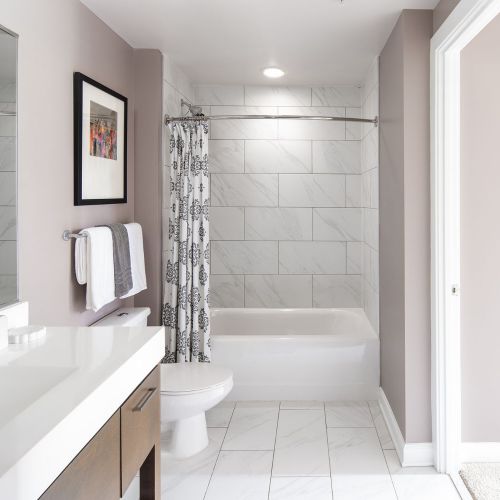 Sleek bathrooms featuring linen tiling and Carrara marble vanities