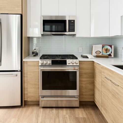 The modern design palette features natural wood & high-gloss white cabinets, glass backsplash, white quartz countertops, and waterfall islands