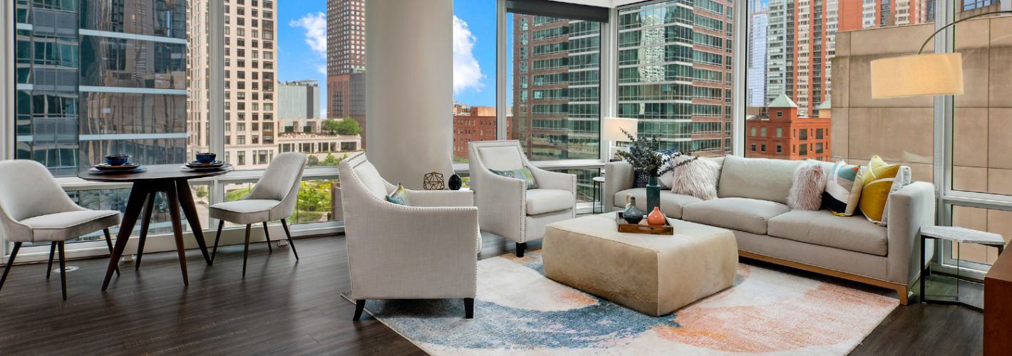 A corner apartment living and dining area flooded with natural light from floor-to-ceiling windows.