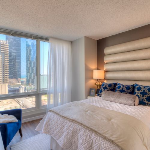 Wide angle of a decorated bedroom with a charcoal accent wall and large windows.