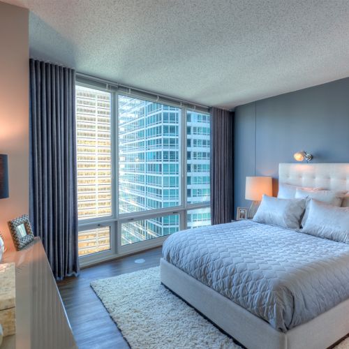 Wide angle of a decorated bedroom with a charcoal accent wall and large windows.