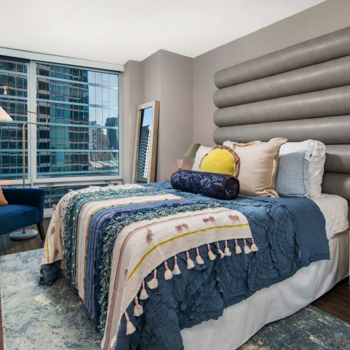 Close up of a bedroom with luxury bedding, a dresser, large artwork, and comfortable seating. 