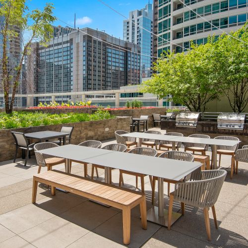 Wide angle of Atwater's sundeck, private outdoor grill area, and patio furniture with foliage and the cityscape in the background.