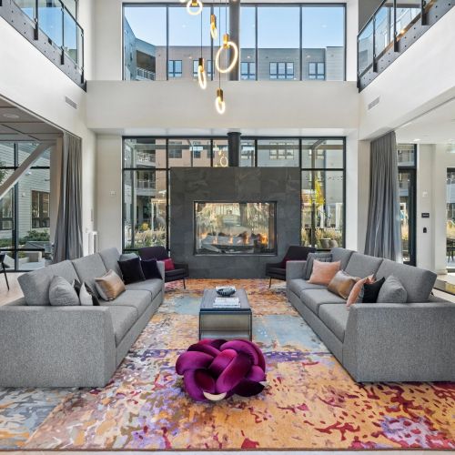 Double-height lounge with gray sofas, fireplace, colorful rug, and large modern windows