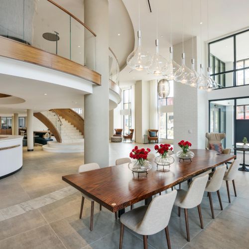 Elegant lobby with modern chandelier, curved staircase, and communal wood table
