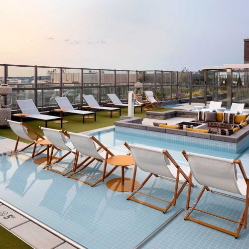 Rooftop pool with in-water lounge chairs, cabana seating, and turf sun deck at sunset