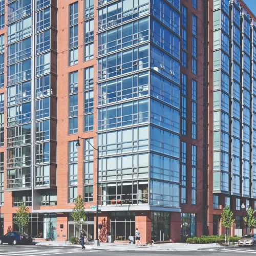 Modern mid-rise apartment building with red brick and large glass windows on city street