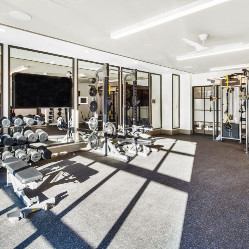 Bright gym with dumbbells, bench press, cable machines, and floor-to-ceiling mirrors