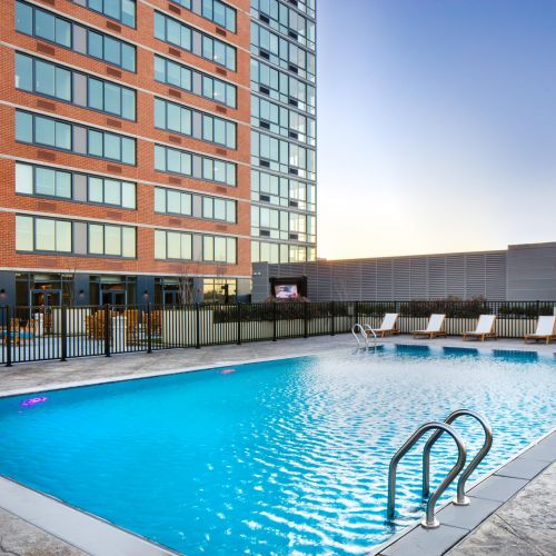 Outdoor pool with lounge chairs and metal fence beside red brick mid-rise at sunset