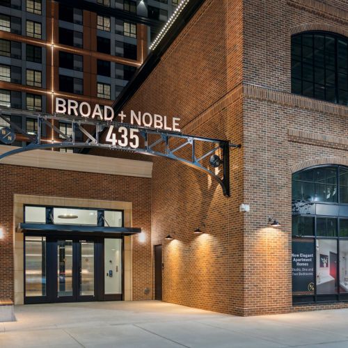 Broad + Noble 435 brick building entrance with large sign and lit storefront windows