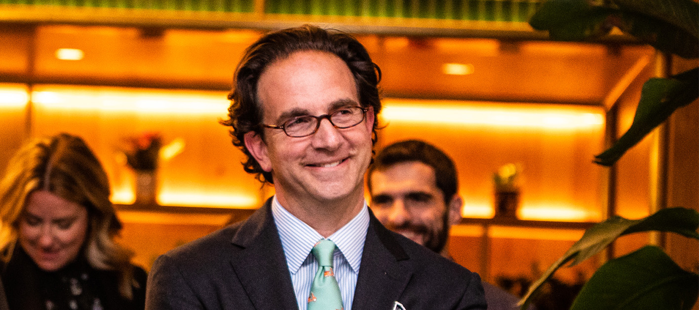 CEO Toby Bozzuto smiling at the camera with some people in his background.