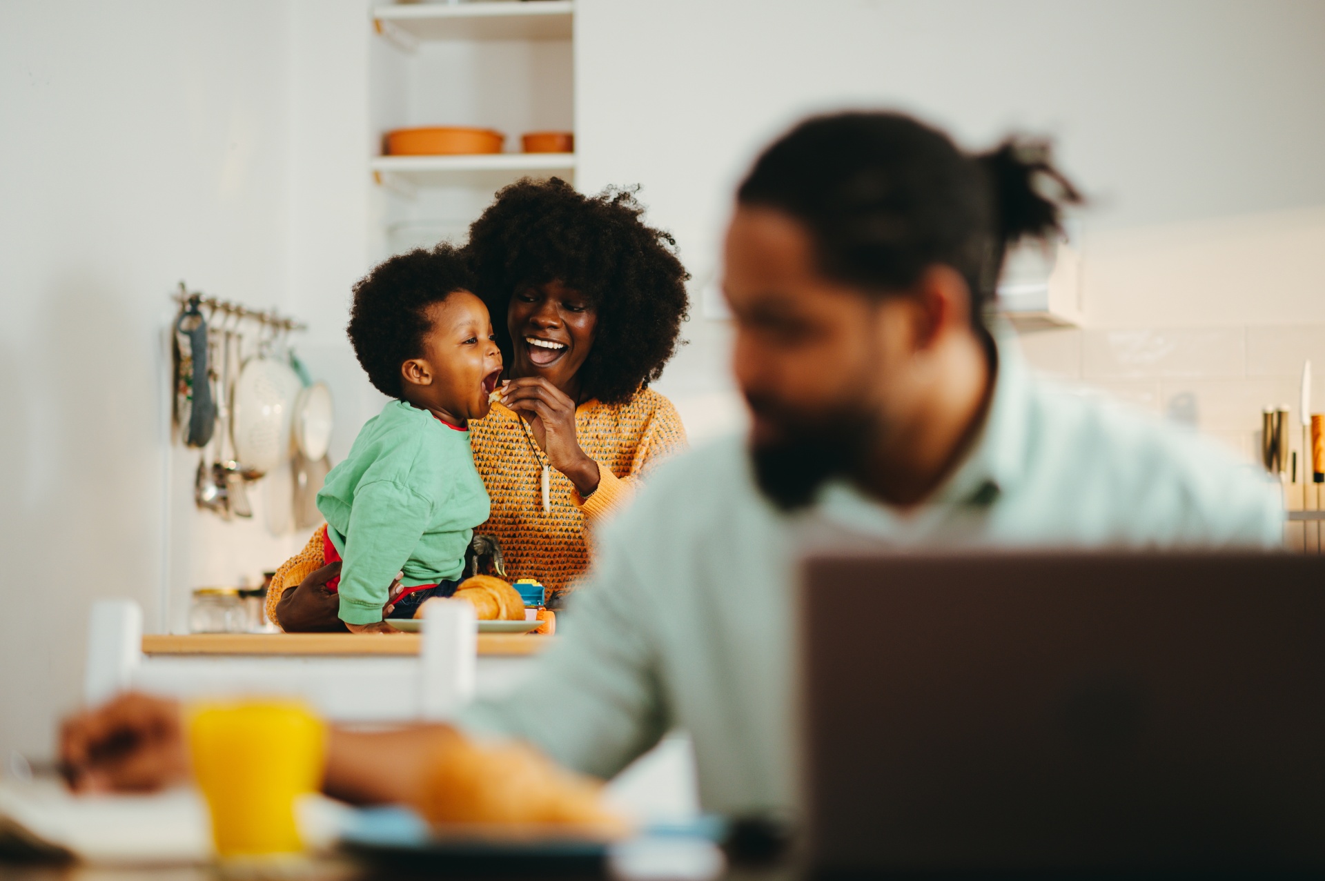 Man working on his laptop with a woman & child sharing a happy meal in the background