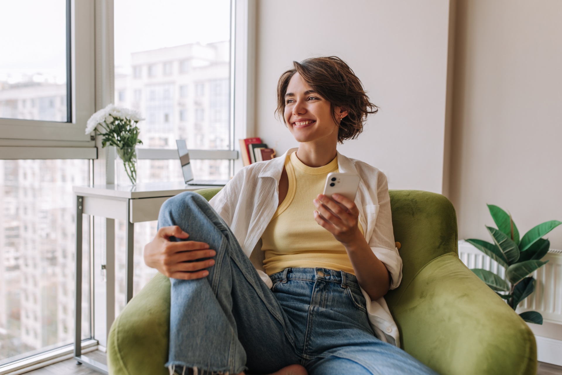 Smiling woman holding her phone & sitting in a chair in a bright room