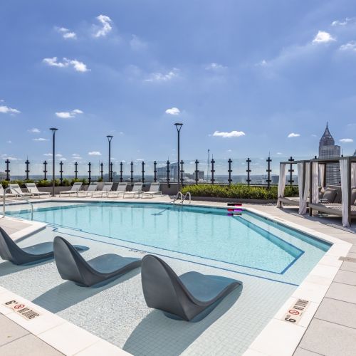 rooftop pool with lounge chairs, daybeds, and skyline views under a clear blue sky