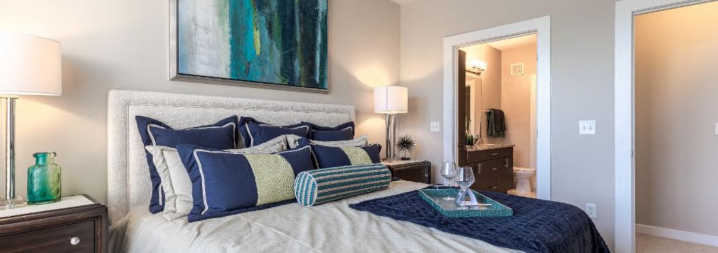 Photo of bedroom showing a bed filled with throw pillows and artwork above the headboard