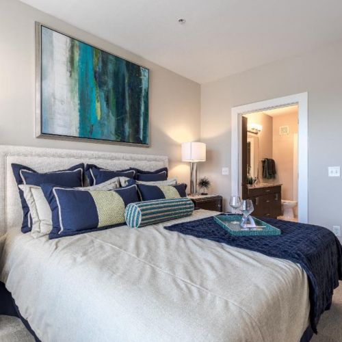 Photo of bedroom showing a bed filled with throw pillows and artwork above the headboard