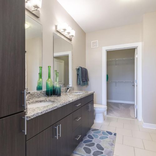 Photo of well lit bathroom with tiled floors and his/her sinks, multiple cabinets and a walk-in closet in the back