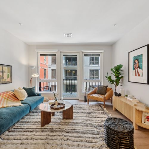 Modern living room with emerald sofa, open kitchen, island seating, and woven wall art