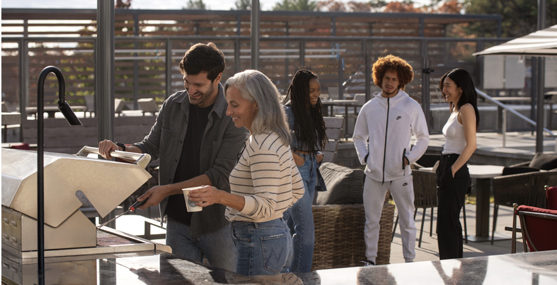 People grilling and talking on a rooftop patio.