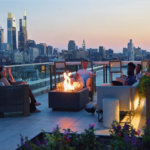 Group sitting around a rooftop fire pit at sunset.